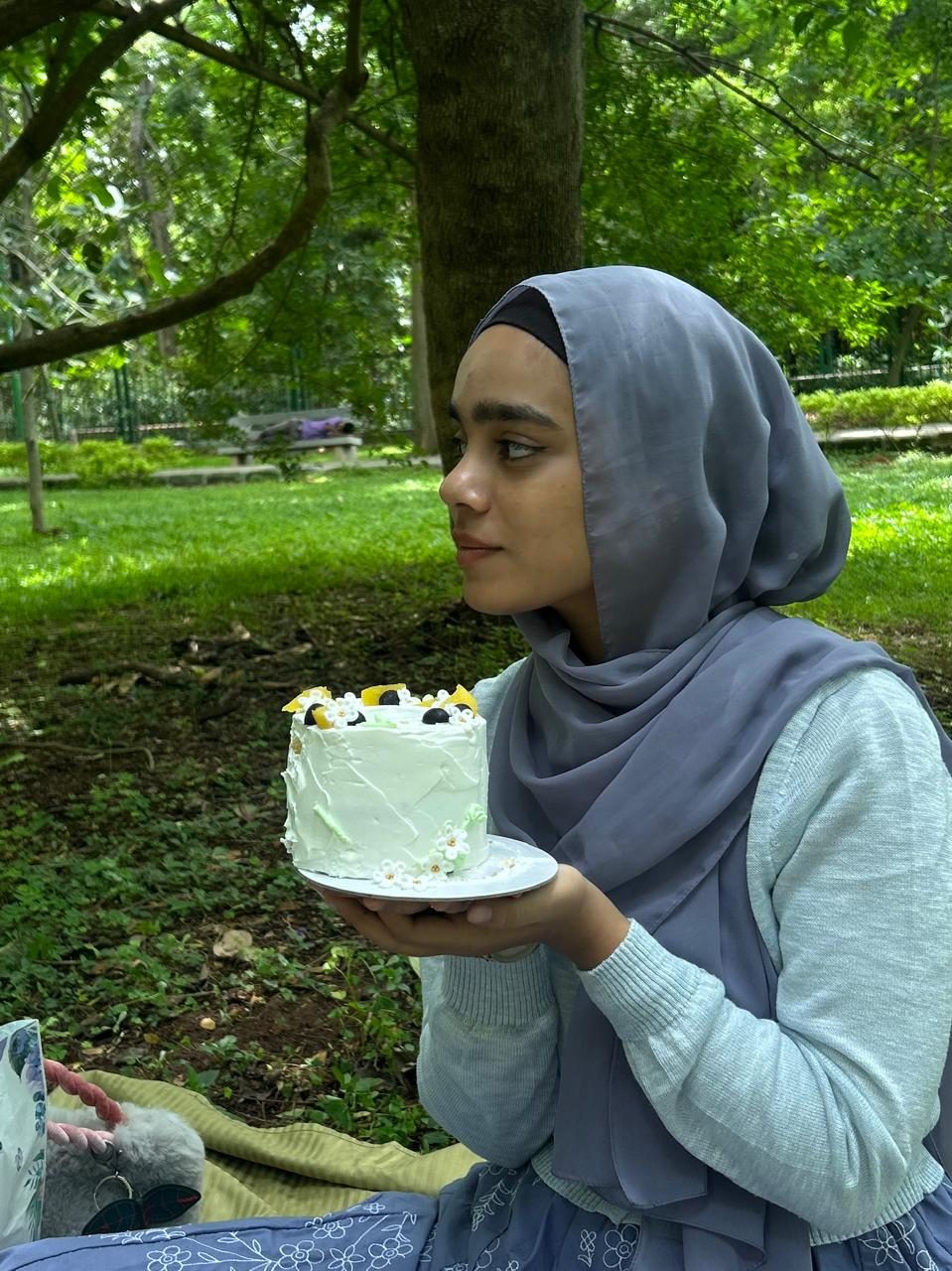 Arfa holding a small white cake under a tree